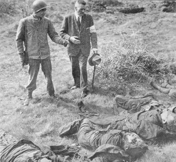 Ein US-Soldat zeigt Anfang Mai 1945 dem Warsteiner Bürgermeister Peter Struif die 71 Leichen der im Langenbachtal ermordeten Menschen (Repro Archiv P. Bürger; Aufnahme von U. Hillebrand in den 1980er Jahren bei der US-Army angefordert). 
