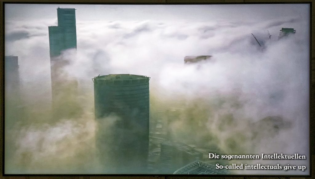 Hochhäüser bzw. hohe runde Industrietürme im Rauch/Nebel(Wolken). Unten rechts stehen die Zeilen: 
Die sogenannten Intellektuellen
So-called intellectuals give up 