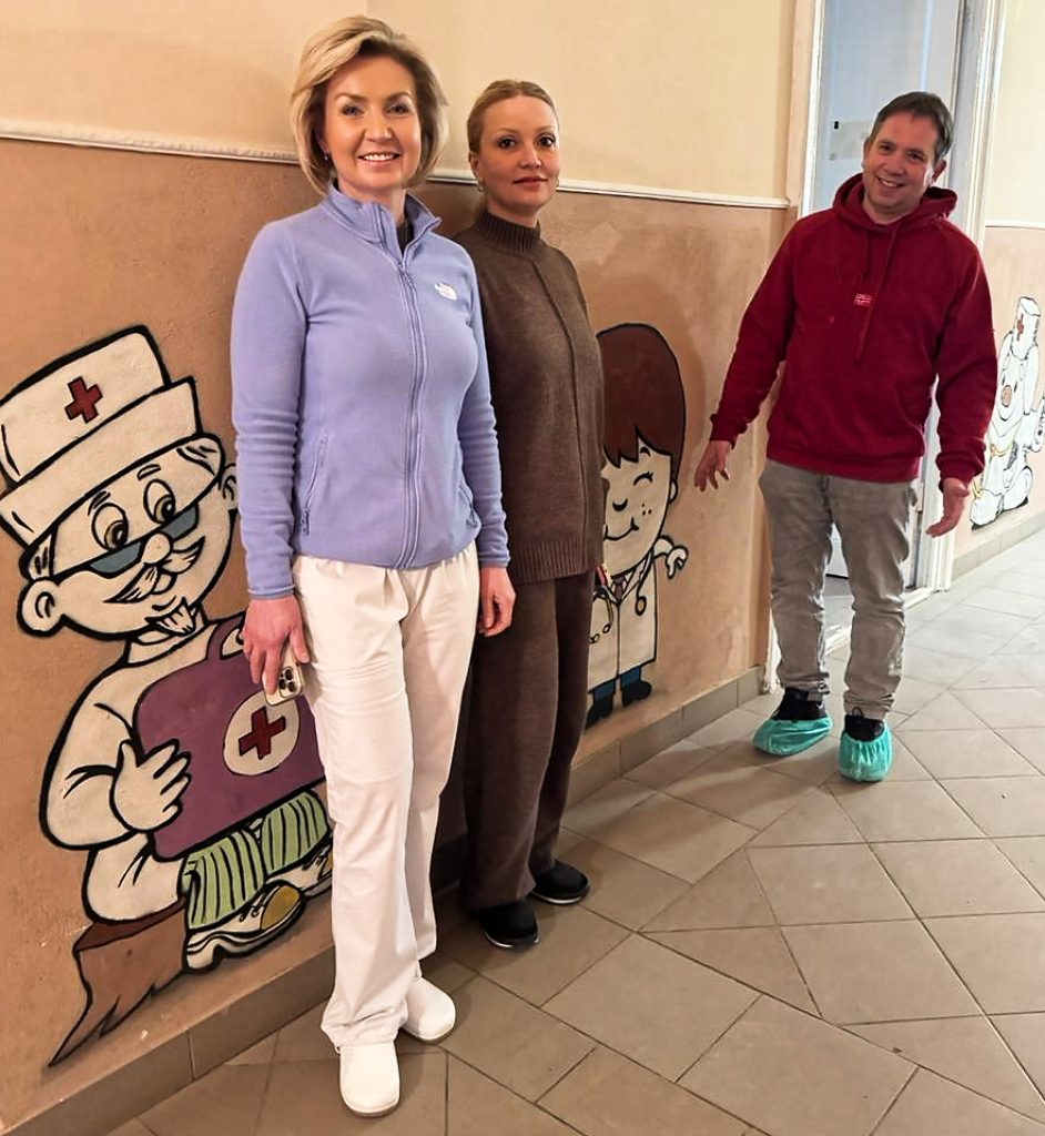 Zwei Frauen und ein Mann im Gang der Kinderabteilung. Kindgerechte Wandmalereien, Zeichnungen: Ärzt*innen